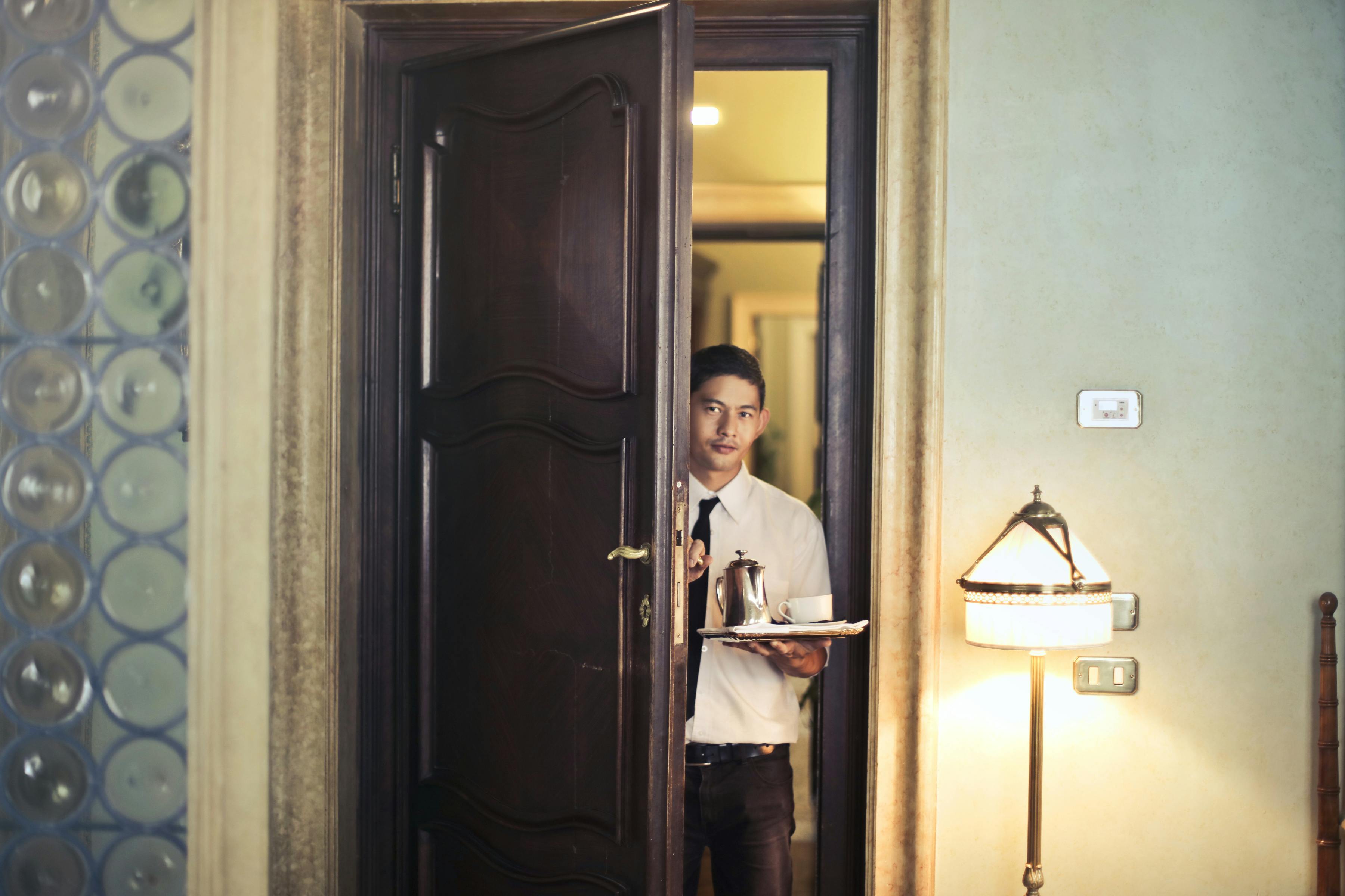 A room-service waiter entering a guest room — the frontline moment hospitality runs on, repeated thousands of times a night at scale.