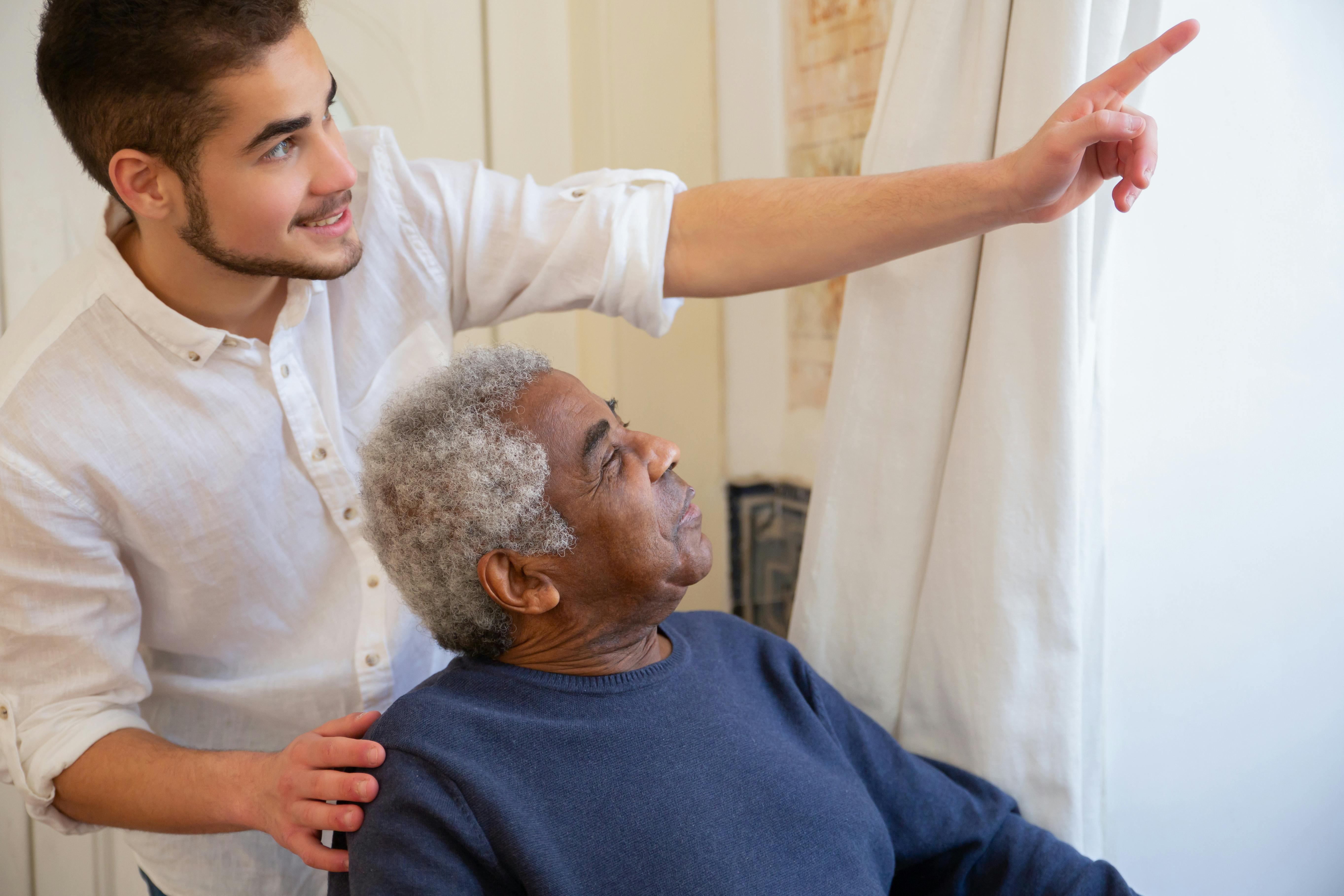 A caregiver and a senior resident in mid-conversation, near a sunlit window. Documentary, warm available light.