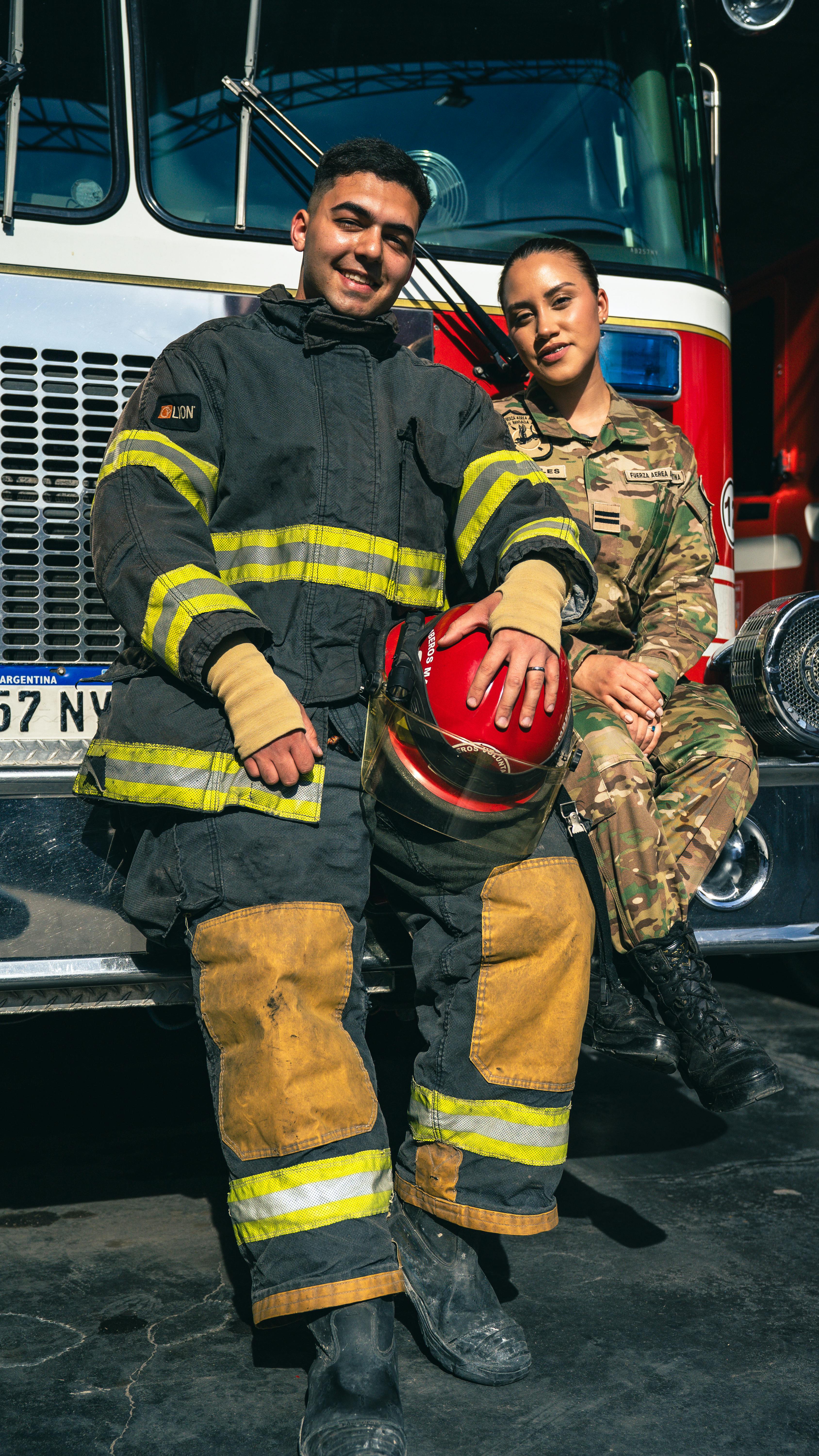 A firefighter and a service member standing together in front of an emergency vehicle.